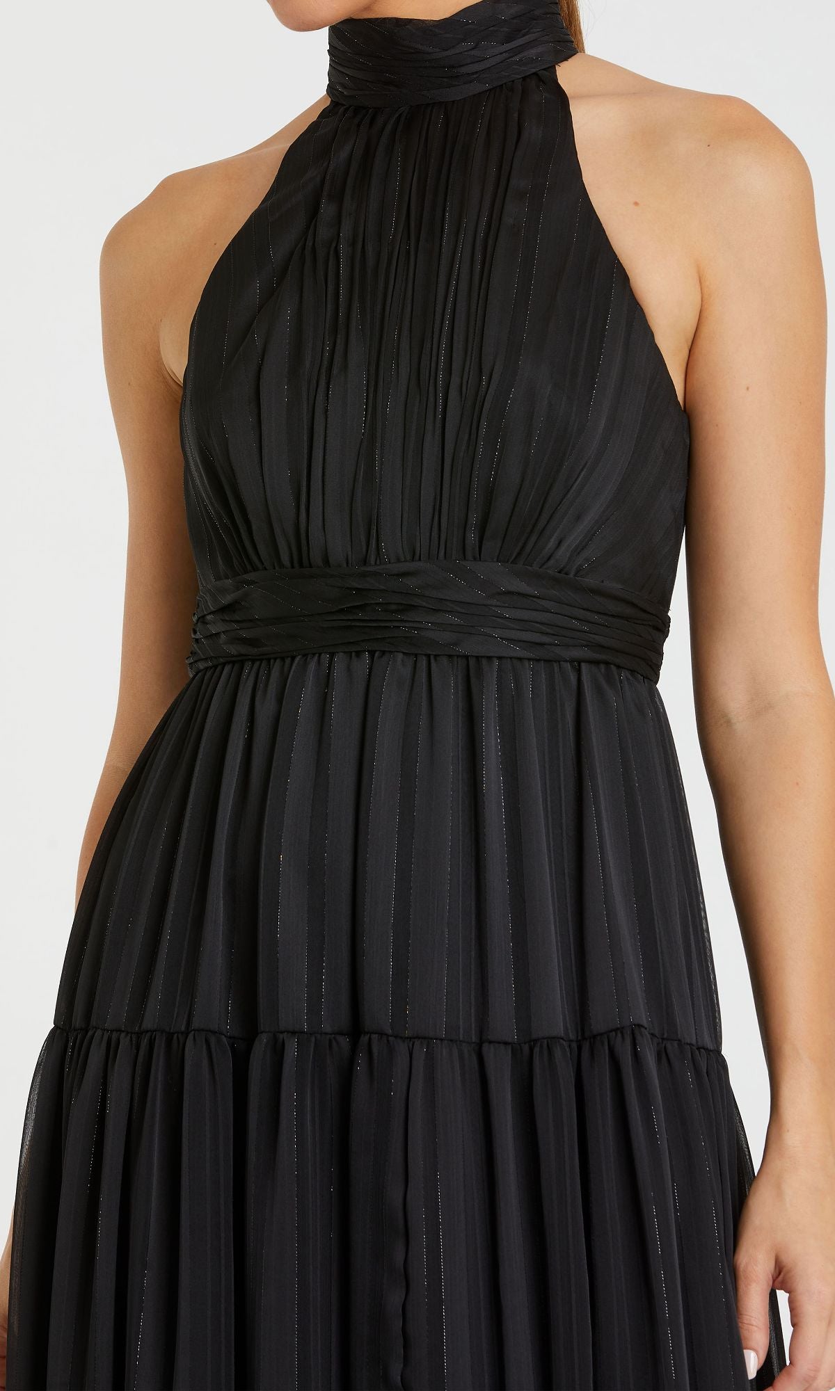 Woman wearing a sleeveless black halter-neck Mac Duggal 49515 dress, featuring pleated fabric and subtle vertical stripes, shown from shoulders to waist.